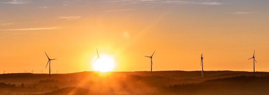Sunrise over fields and hills, wind turbines are situated along the top of a distant hill