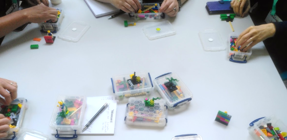 Photograph from above a table upon which various hands can be seen modelling Lego