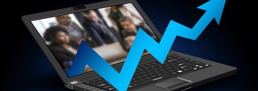 Laptop with image of people in discussion on screen, with graphical representation of a statistics arrow coming out of the screen